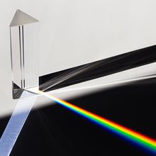 A prism dispersing sunlight, splitting into a spectrum on a white background.