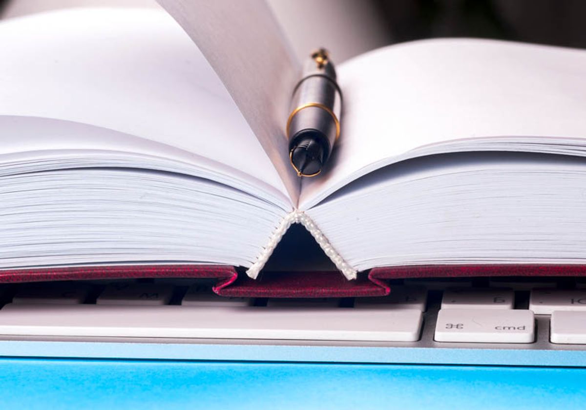 Close up image of an open notebook with blank pages, a computer keyboard, and a pen.