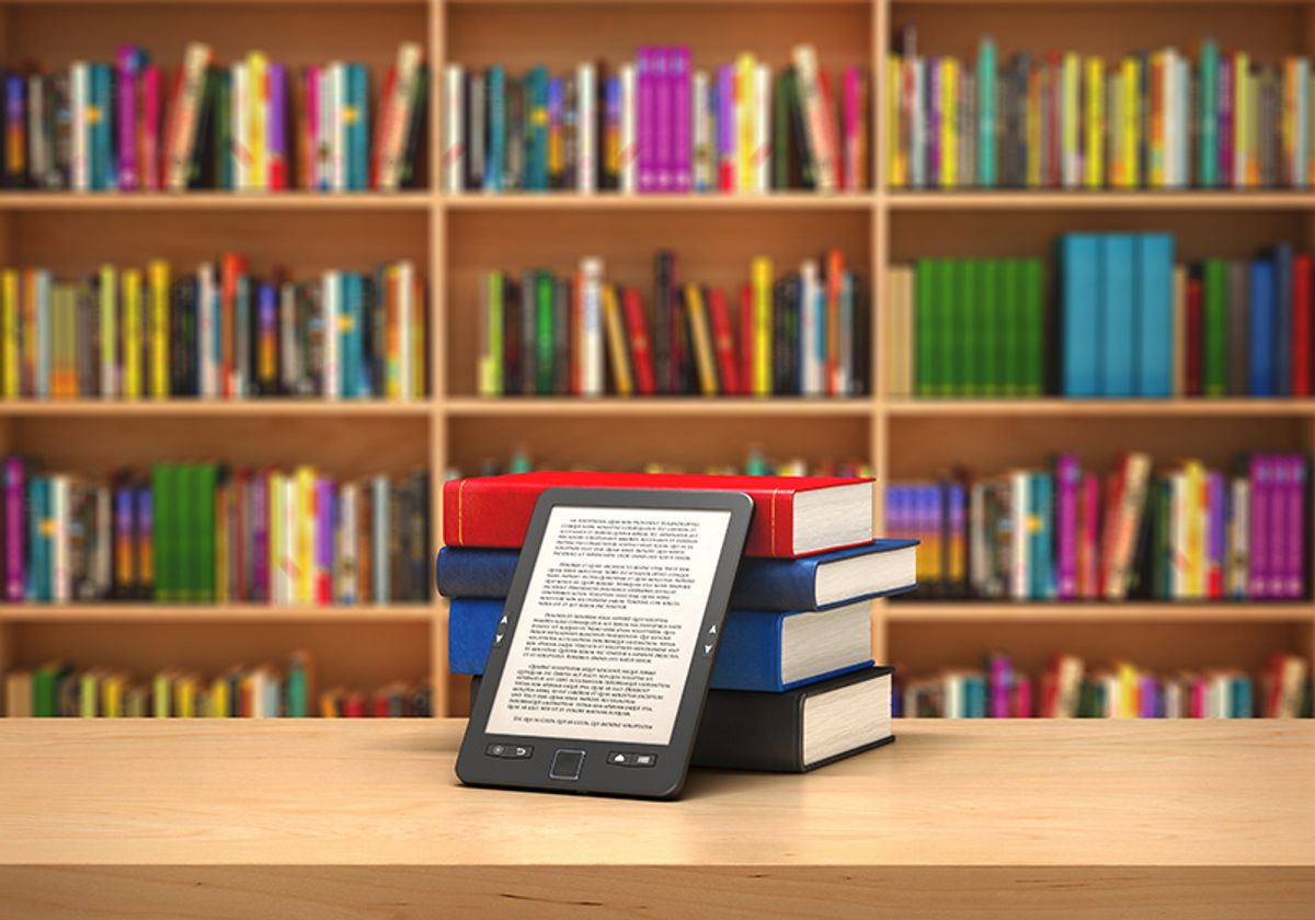 A tablet propped up by a stack of books in front of a bookshelf.