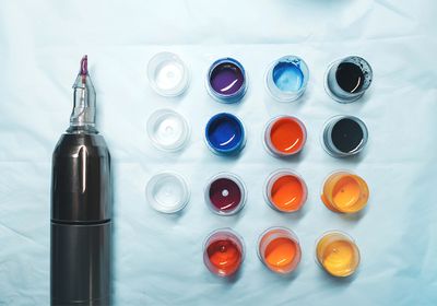 Photograph of the end of a tattoo gun and pots of different colored ink on a napkin.