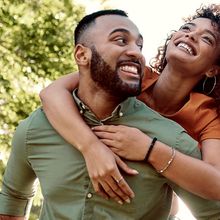 A man in a green shirt gives a woman a piggyback ride outdoors, both are smiling.