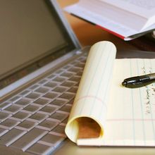 A laptop and a pad of paper with writing on it.