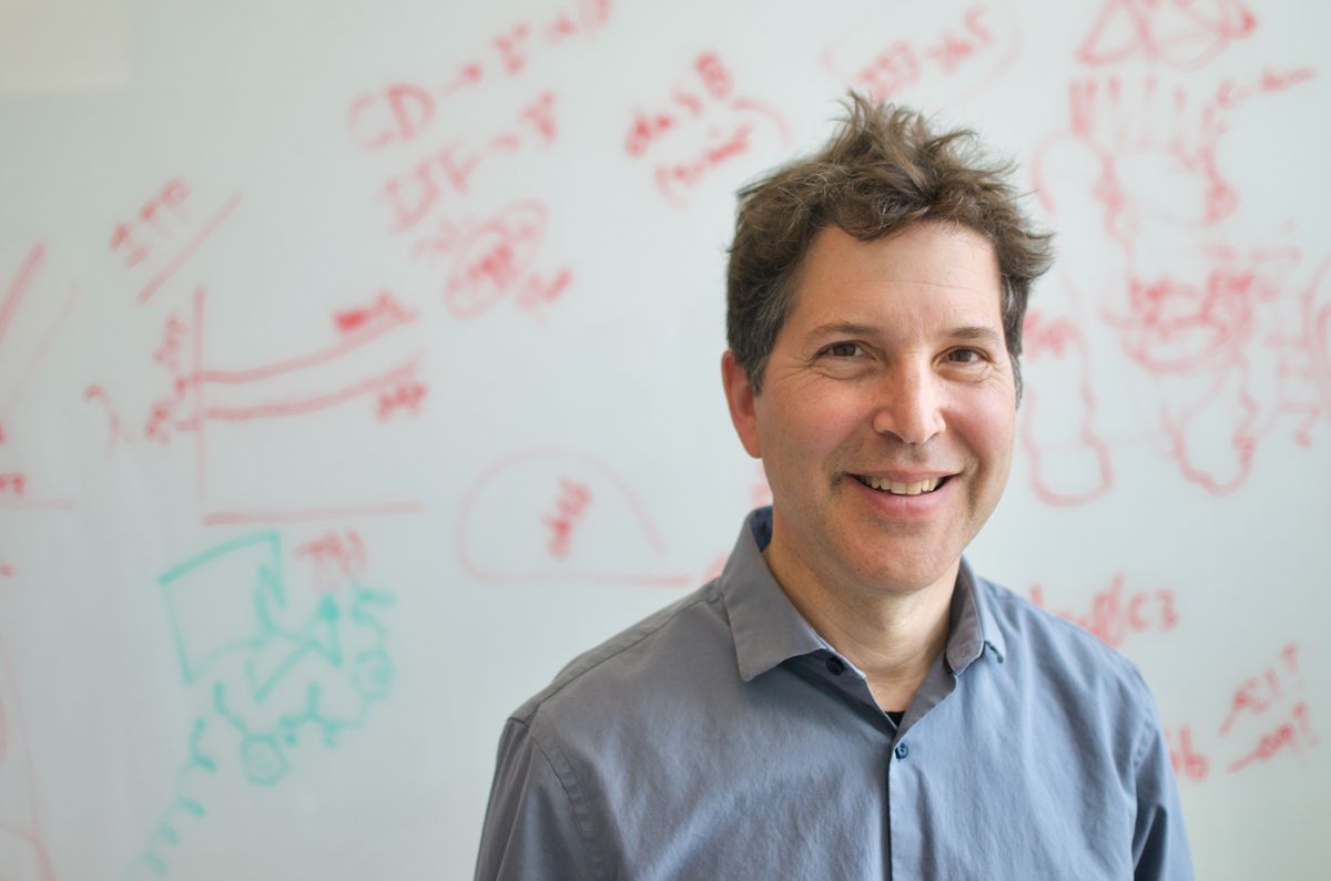 David Baker wears a blue shirt and stands against a whiteboard.