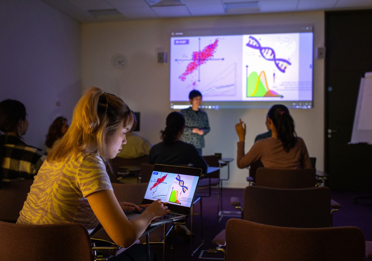 An image of a classroom where a scientist is giving a presentation using a slide deck projected on the wall.