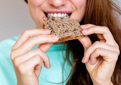 A woman eating a piece of multigrain bread.