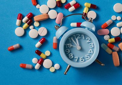 Some pills strewn about next to an alarm clock on a blue background.&nbsp;