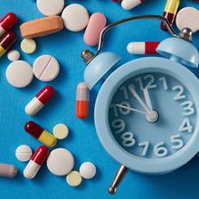 Some pills strewn about next to an alarm clock on a blue background.&nbsp;