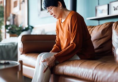 Middle aged woman sitting on a sofa, holding her knee in pain.