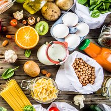 Zero waste shopping and sustainable lifestyle concept photograph of vegetables, grains, pasta, eggs and fruits in reusable packaging on a wooden panel background.