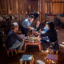 Matthieu Groussin sits with three other people on stools in front of a low table, on which there are several bowls of food. Another person stands above Groussin spooning something into a bowl.