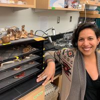 Adriana L. Romero-Olivares kneels in the lab next to dry mushrooms in oven.