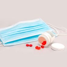 A surgical mask next to an open pill bottle that&rsquo;s toppled over, spilling out red capsules meant to represent vitamin D supplements.