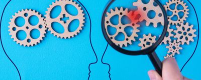 Two drawn heads on a blue background with gears in their heads. A red spot on two gears is magnified over one head.