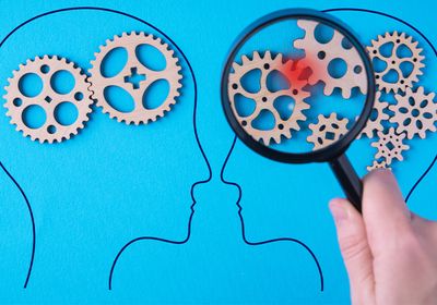 Two drawn heads on a blue background with gears in their heads. A red spot on two gears is magnified over one head.