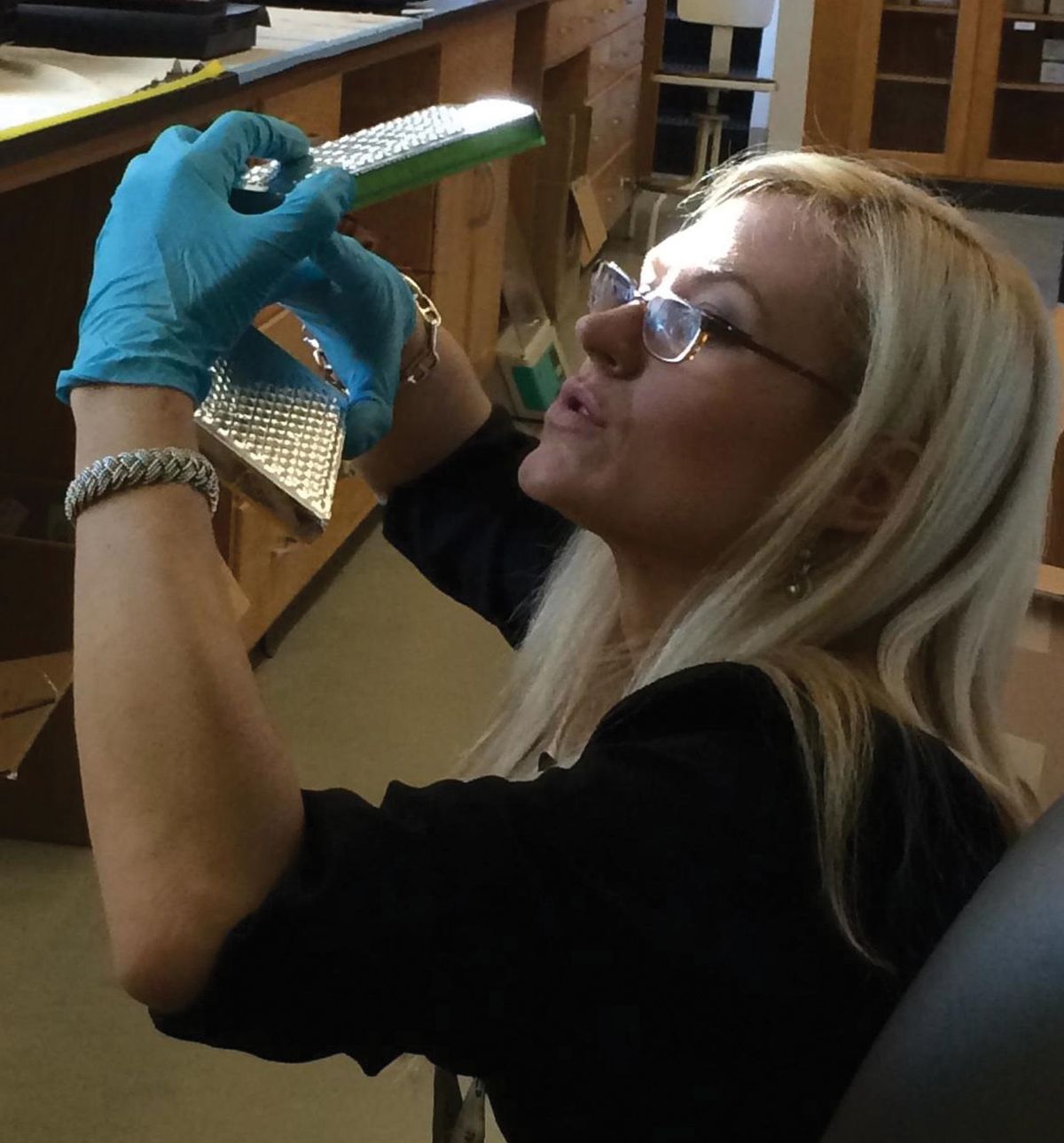 Image of microbiologist Anne Madden holding up environmental DNA samples of house dust.