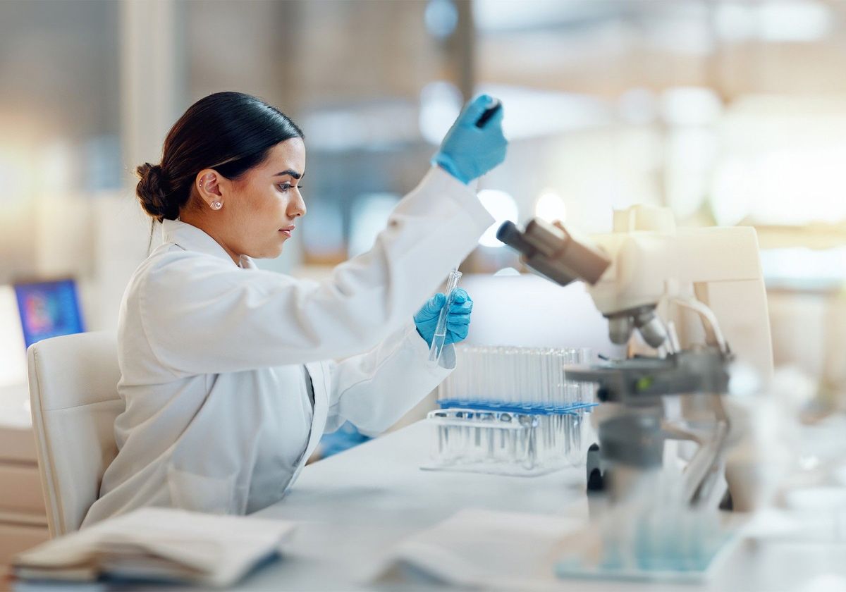 An individual working at a scientific bench in front of a microscope.