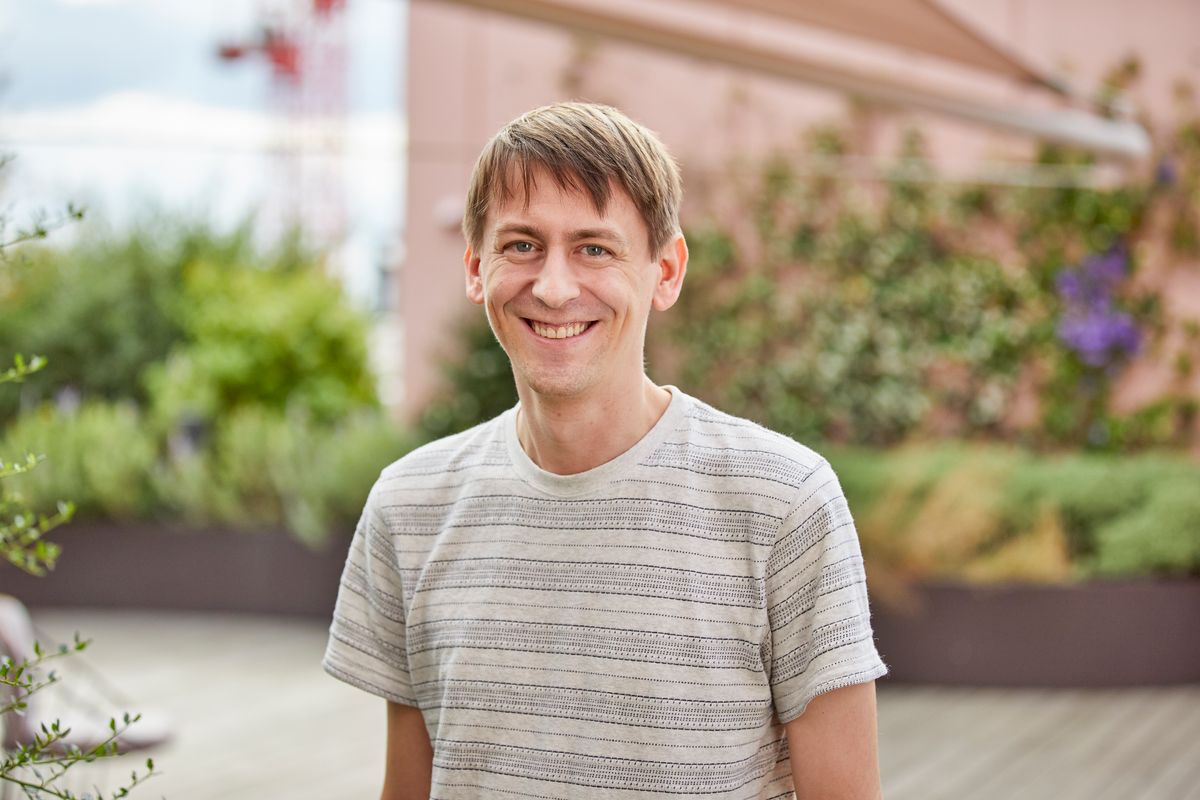 Headshot of John Jumper. He smiles at the camera and is wearing a striped shirt.