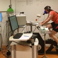 a young woman pedals an exercise bike while wearing a mask to monitor oxygen consumption