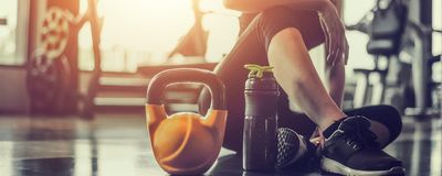 A person sitting in a gym with a protein shake bottle and kettlebell placed beside them.