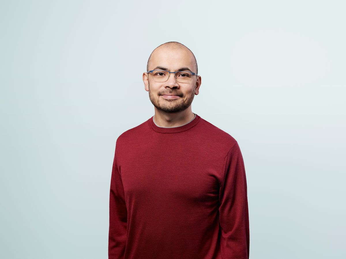 Headshot of Demis Hassabis. He wears glasses and a red sweater.