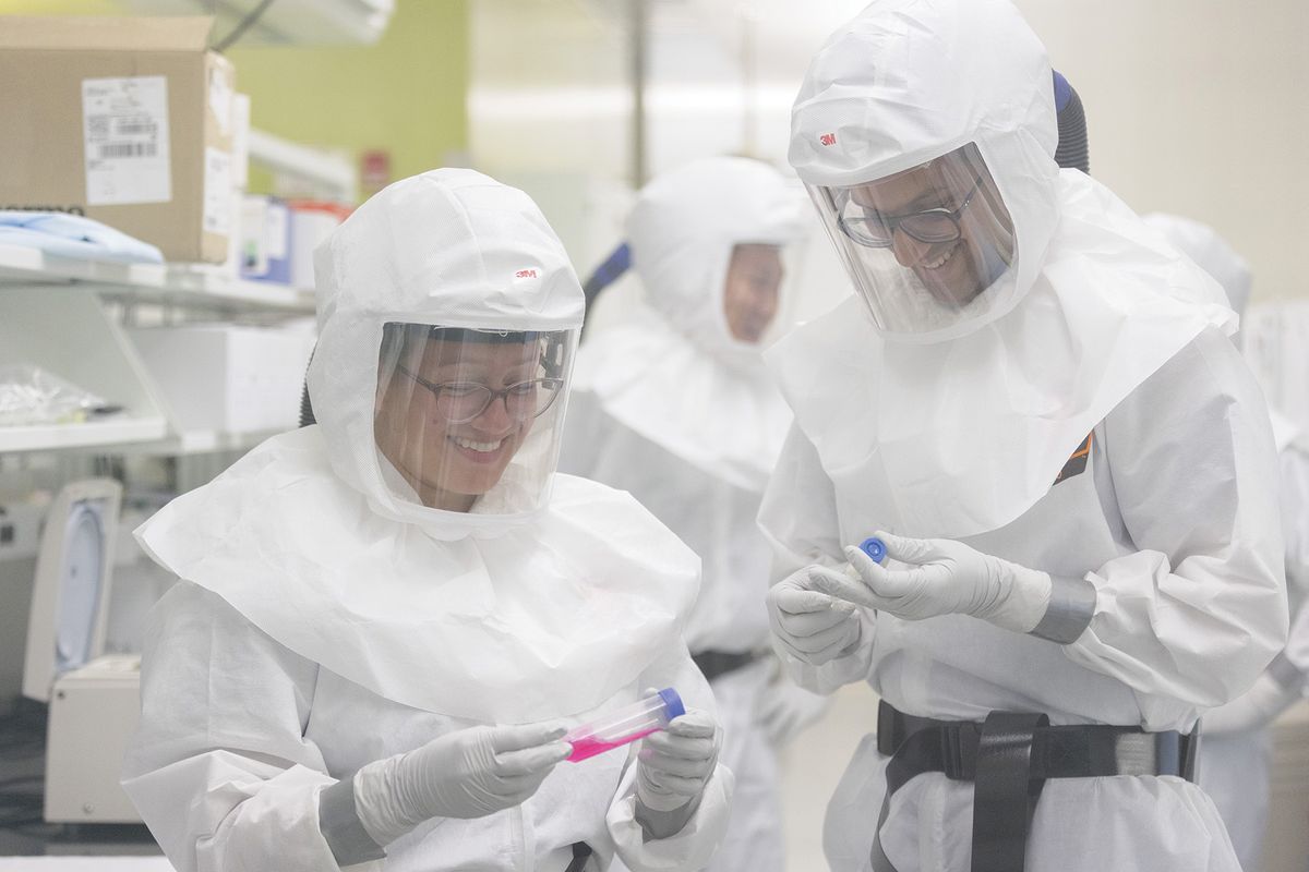 Arinjay Banerjee and a fellow researcher wear white suits with clear face plates and hold test tubes.