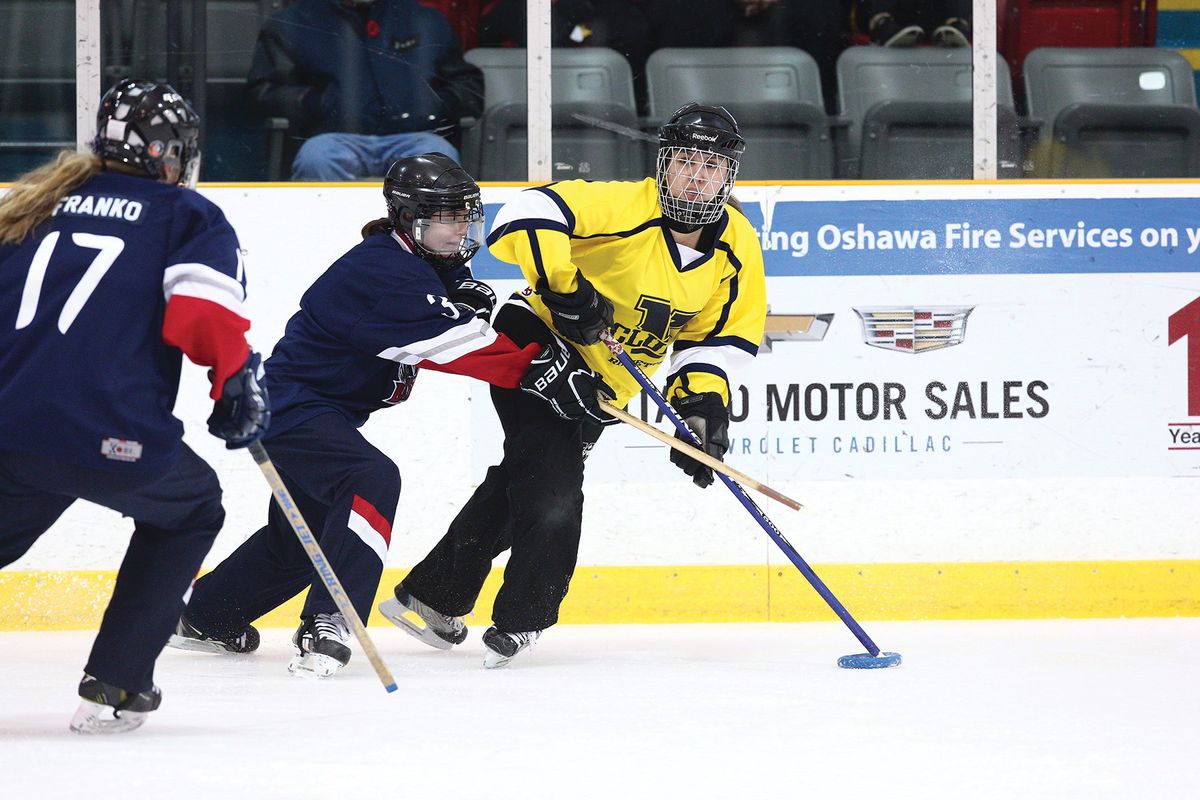 Image of three ringette players on an ice rink. Two players are in blue, red, and white jerseys. Melissa Kay is pictured in the yellow jersey.