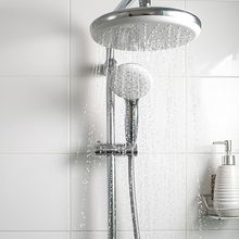 Image of a showerhead with running water. There is a soap dispenser and toothbrush on a wire shelf in the shower.