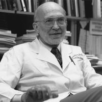 Black and white image of Jean Wilson in an office, wearing a lab coat.