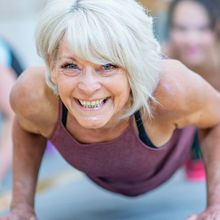 Woman smiling at the camera working out on a blue yoga mat.