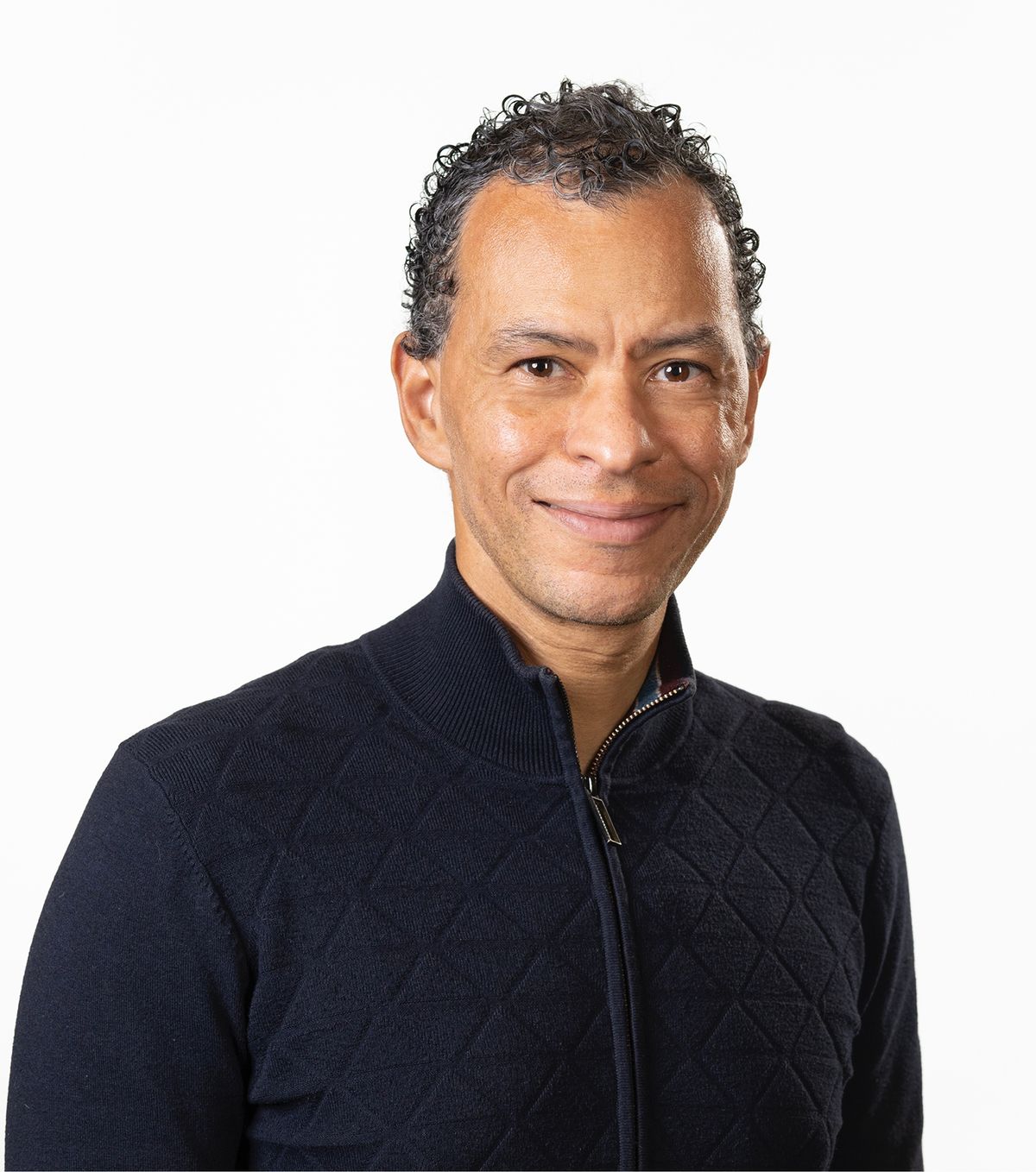 Image of Lloyd Trotman. He wears a navy jacket and smiles at the camera against a white background.