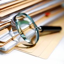 Magnifying glass in front of a stack of files of papers