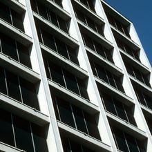 the facade of a building. crisscrossed white walls intersect sets of four black windows in a lattice structure, with a cloudless blue sky in the background.