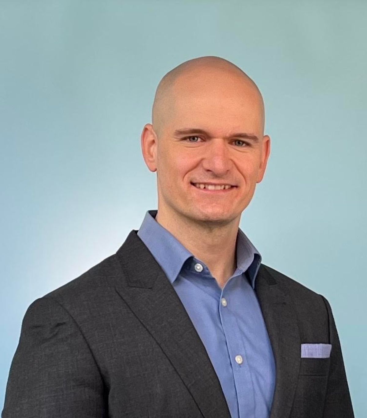 David Olson, a chemical neuroscientist and director of the Institute for Psychedelics and Neurotherapeutics at the University of California, Davis poses for a photo on a light blue background, wearing a blue shirt and black blazer.