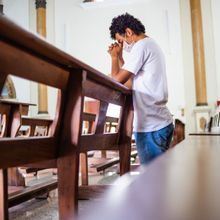 a man kneels at a pew, praying