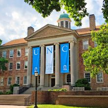 Brick building with white pillars and three banners spelling "UNC"