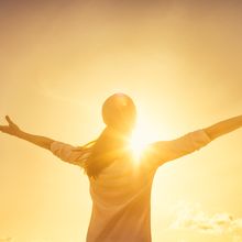 Woman with her back to camera, with arms stretched out, soaking up the sunshine