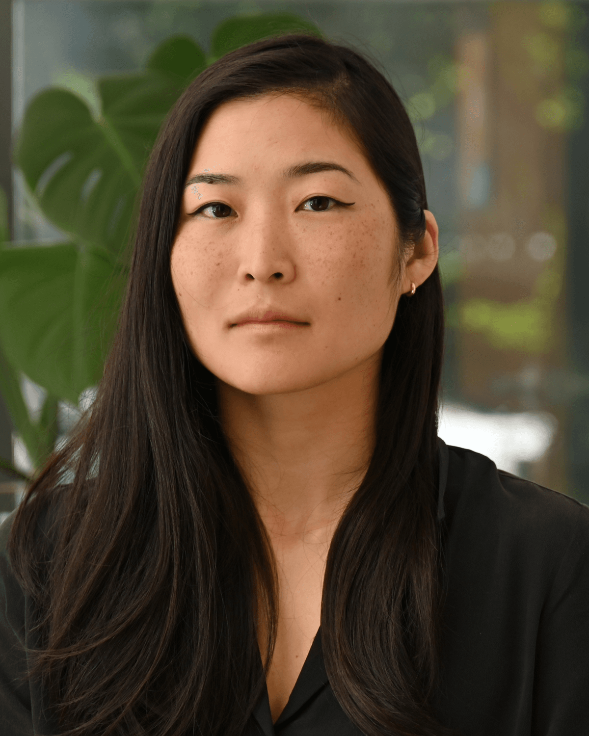 Christina Kim, a neuroscientist and bioengineer at the Institute for Psychedelics and Neurotherapeutics at the University of California, Davis poses for a photo wearing a black shirt, with a plant in the background.